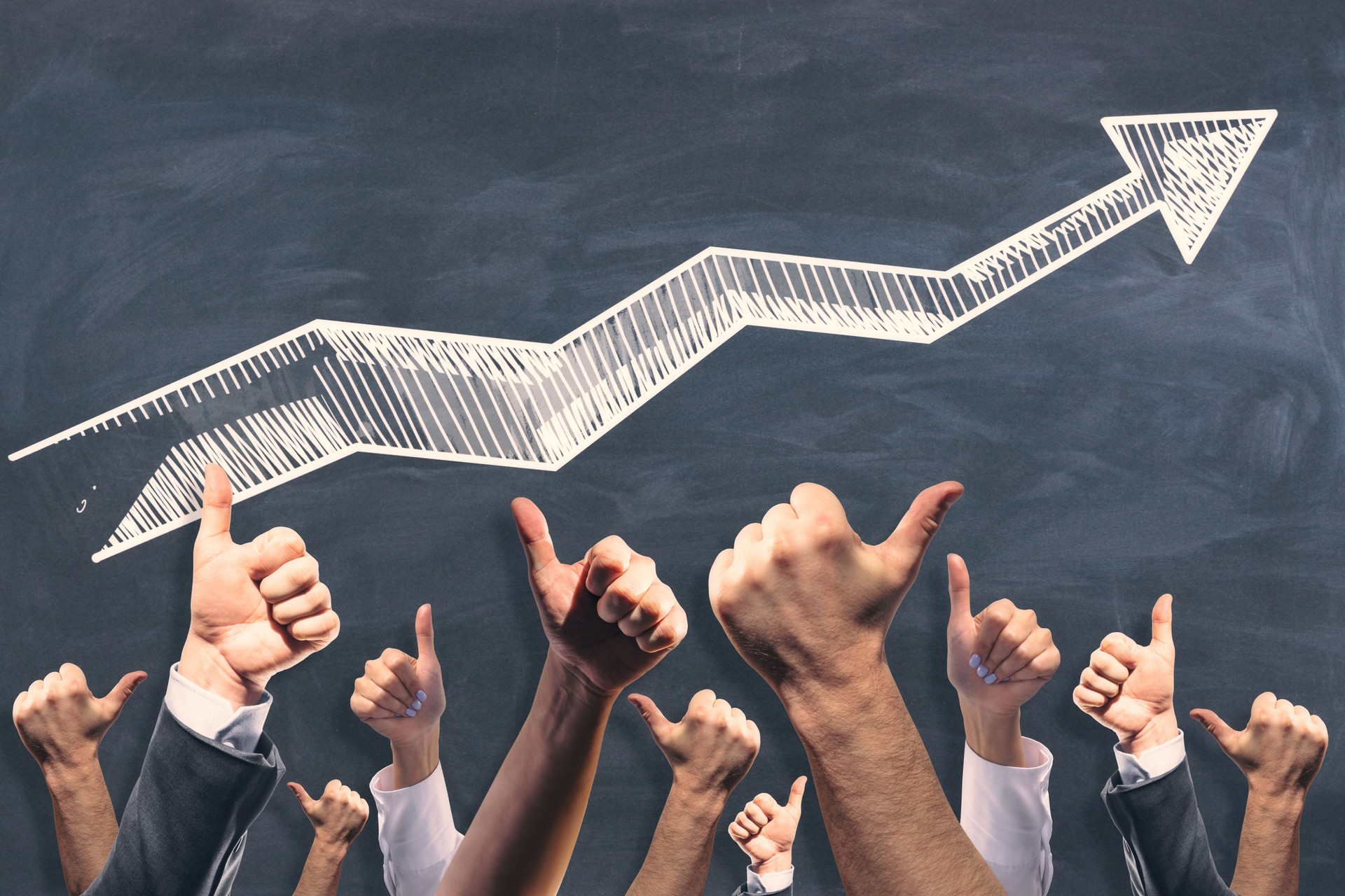 Various male and female hands showing thumbs up on chalkboard wall background with growing arrow.
